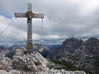 Vrcholový kríž na Monte Paterno (2744 m) a trpiteľský výraz horolezca, ktorý sa zrazu ocitne na kábloch preplnej feraty